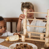 Zwei Kinder spielem mit Grapat Woodland Bausteinen und Holzleisten. Davor auf dem Tisch stehen Teller mit Kuchen und Nussschalen.