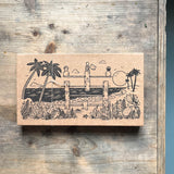 Eine Schachtel aus braunem Karton mit einer in schwarz gemalten Landschaft. Bauwerke und Konstruktionen auf denen Männchen stehen sind abgebildet.