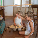 Zwei Kinder spielen mit Grapat "The Pendulum" - eine an einem Stab baumelnde Holzplatte. Ein Junge versucht eine Kugel auf der Platte abzustellen.