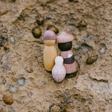 3 Spielfiguren aus Holz in den Farben braun und rosa der Grapat Lucky Lucky 3. Edition Überraschungsboxen stehen auf einem Stein.