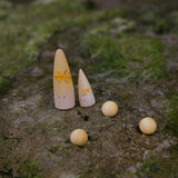 2 Spielfiguren aus Holz in den Farben gelb und rosa und drei kleine Holzmurmeln der Grapat Lucky Lucky 3. Edition Überraschungsboxen sind auf einem Stein platziert.