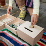 Ein Kind spielt mit der Grapat "Permanence Box" und versucht, ob eine kleine Spielfigur aus Holz durch das Loch passt. Daneben sind andere Materialien zum Versuchen angeboten.