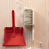 Ein kleiner Handbesen aus Holz und eine kleine, rote Kehrschaufel aus Metall.