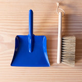 Ein kleiner Handbesen aus Holz und eine kleine, blaue Kehrschaufel aus Metall.