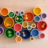Viele verschieden farbige und verschieden große Holzbecher der Grapat "Nest Bowls" sind kunterbunt zusammengestellt und teilweise befüllt mit Mandala Material und Nins Holzfiguren zum Spielen.