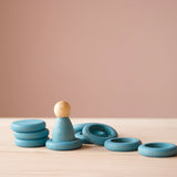 Eine blaue Spielfigur "Nins" aus Holz von Grapat in einem blauen Holzring, daneben liegen weitere 5 blaue Ringe und drei Holzplättchen.