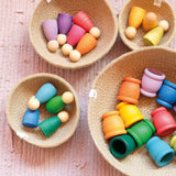 Vier verschieden große Körbchen, darin sind Grapat Nins Holz Spielfiguren und Holzbecher in Regenbogenfarben verteilt.