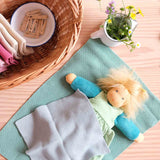 Das Puppenkind Lotti liegt unter einem Stricktuch zugedeckt, daneben ein Milchkännchen mit frischen Blumen und ein Korb mit Tüchern und Wäscheklammern.