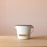 Weißer kleiner Eimer zum spielen für Kinder aus Emaille mit einem Holzgriff am Henkel.