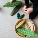 Papoose grüne Erbsenschoten aus Filz zum Bespielen liegen in einem Korb und rundherum.