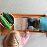 Blick von oben auf ein Holztischchen mit grünen Filz-Erbsenschoten, Filtüchern und ein Kuscheltier.