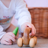 Ein Baby hält das Greifauto von Kokomoo in der linken Hand, rechts hält es eine grüne Spielfigur aus Holz.