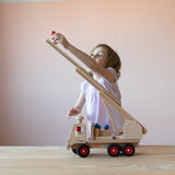 Ein Kind spielt mit dem Fagus Feuerwehr Auto, das Holzmännchen ist ganz hoch oben auf die ausgefahrene Drehleiter geklettert.