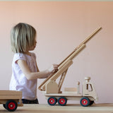 Ein Kind spielt mit dem Fagus Feuerwehr Fahrzeug, die Drehleiter wird gerade von ihm ausgefahren, daneben steht ein Fagus Anhänger.