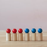 Drei Holzfiguren von Fagus mit rotem Kugelkopf, drei mit blauem Kopf stehen in einer Reihe nebeneinander.