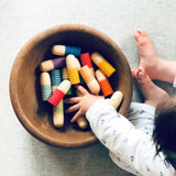 Die bunten Spielfiguren Grapat Brots liegen in einer Holzschale, ein Baby greift mit der Hand hinein.