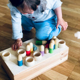 Ein Kind stützt sich mit Knie und Hand auf eine Holzkiste, auf der Grapat Brots und Holzringe zum Spielen verteilt liegen.