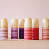 Sechs Grapat Bots Spielfiguren aus Holz in rot-, rosa- und lila-Tönen stehen nebeneinander aufgereiht.