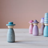 Vorne steht eine Grapat Fancy Nins Spielfigur in Blau mit einem farblich passendem Hut, im Hintergrund weitere Spielfiguren aus Holz in Blau, Lila und Rosa.