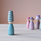 Vorne steht eine Grapat Fancy Nins Spielfigur in Blau mit einem farblich abgestimmten Hut, im Hintergrund weitere Spielfiguren aus Holz in Blau, Lila und Rosa.