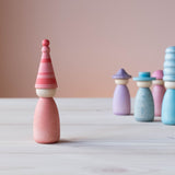 Die rosa Spielfigur aus Holz mit farblich passendem rosa-gestreiften Hut vorne, hinten stehen Grapat Fancy Nins in Blau- und Lilatönen.
