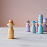 Vorne steht eine Grapat Fancy Nins Spielfigur in gelb mit einem gelb-orangem Hut, im Hintergrund weitere Spielfiguren aus Holz in Blau- und Lilatönen.