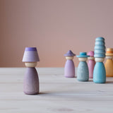 Vorne steht eine Grapat Fancy Nins Spielfigur in lila mit einem farblich passendem Hut, im Hintergrund weitere Spielfiguren aus Holz in Blau- und Lilatönen.