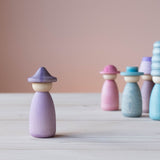 Vorne steht eine Grapat Fancy Nins Spielfigur in lila mit einem gleichfarbigem Hut, im Hintergrund weitere Spielfiguren aus Holz in Blau, Lila und Rosa.