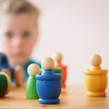 Die blaue und die gelbe Holzspielfigur "Nins von Grapat" stecken in die Holztöpfchen in den gleichen Farben.