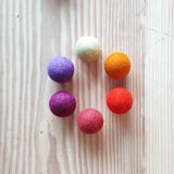 Sechs Filzbälle "Sonne" von Kokomoo in weiß, orange, rot, rosa, violett und lila im Kreis aufgelegt.