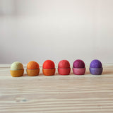 Sechs Filzbälle "Sonne" von Kokomoo in weiß, orange, rot, rosa, violett und lila in farblich passenden Holztöpfchen von Grapat in einer Reihe aufgestellt.