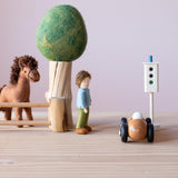 Kleine Welt Spiel mit Spielmaterialien aus Holz und Filz: ein kleines Filzpferd hinter einem Weidezaun aus Holz, daneben ein Filzbaum mit grüner Krone, ein Filzpüppchen, ein Holzauto und eine kleine Ampel aus Holz.