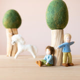Zwei Filzbäume mit grüner Baumkrone, zwei Filzpüppchen lehnen sich an seinen Stamm, im Hintergrund ein weißes Filzpferd - eine Szene aus dem Kleine Welt Spiel.