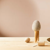 Ein Filzbaum Winter mit weißer Baumkrone aus Filz und einem Stamm aus Treibholz, daneben weiteres Spielmaterial aus Holz.