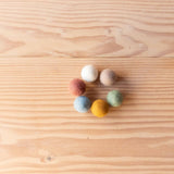 Sieben kleine Filzkugeln von Papoose Toys in verschiedenen Farben im Kreis aufgelegt.