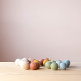 Viele kleine Filzkugeln in Erdtönen von Papoose Toys liegen auf dem Holzboden.