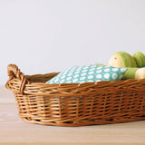 Der ovale, flache Weidenkorb wird für eine kleine Stoffpuppe mit grüner Mütze zum Puppenbett.