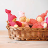 Drei kleine, weiche Stoffwichtel von Nanchen in pink und rosa sitzen in einem flachen Weidenkorb zusammen.