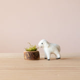 Eine kleine Lamm Spielfigur frisst ihr Futter, nämlich Moos, aus dem Futternapf aus Holz von Drei Blätter.