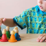 Ein Kind berührt konzentriert einen der bunten Holzfiguren von Grapat. Es stehen 8 bunte Nins vor ihm, jeweils in einem Holzring in der passenden Farbe.