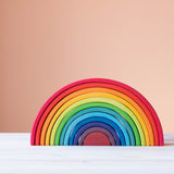 Ein Blick von vorne auf den Grimms Regenbogen original. ganz unten mittig - ein kleines halbrundes Element in weinrot. darueber die Boegen - immer groesser werdend in folgenden Farben: lila, dunkelblau, mittelblau, hellblau, tuerkisblau, lindgruen, gelb, hellorange, dunkelorange, hellrot, kirschrot. Die Boegen sind alle ineinander geschoben woraus sich ein grosser Regenbogen ergibt.