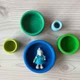 Die fünf Stapelbecher des Grimms Schälchenset "Ozean" einzeln aufgestellt, Blick von oben, im größten, blauen Becher liegt ein kleines Waldorf Filzpüppchen.