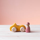 Grimms Holzauto gelb mit Spielfigur aus Holz daneben.