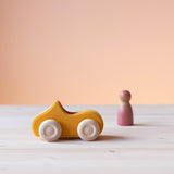 Grimms Holzauto gelb mit Spielfigur aus Holz im Hintergrund.