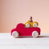 Der große rote Lastwagen von Grimms, darauf stehend das kleine gelbe Holzauto, darin eine Spielfigur.