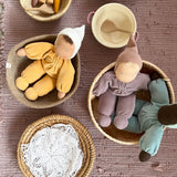 Blick von oben in kleine Körbe: in zwei Körbchen sitzen drei Grimms Kuschelpuppen, in einem sind Häkeldeckchen, in einem anderen Holzspielzeug.