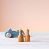 Grimms Holzauto blau, davor zwei gelbe Spielfiguren aus Holz.