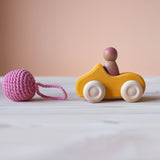 Grimms Holzauto gelb mit Spielfigur aus Holz im Auto, davor ein Häkelball mit Schlaufe von Kokomoo.