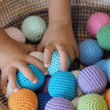 Ein Kind greift mit beiden Händen in einen Korb voll mit Häkelbällen von Kokomoo in verschiedenen bunten Farben.