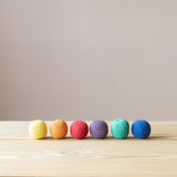 6 Häkelbälle von Kokomoo liegen aneinandergereiht nebeneinander, von links beginnend: gelb, orange, rot, lila, grün, blau.